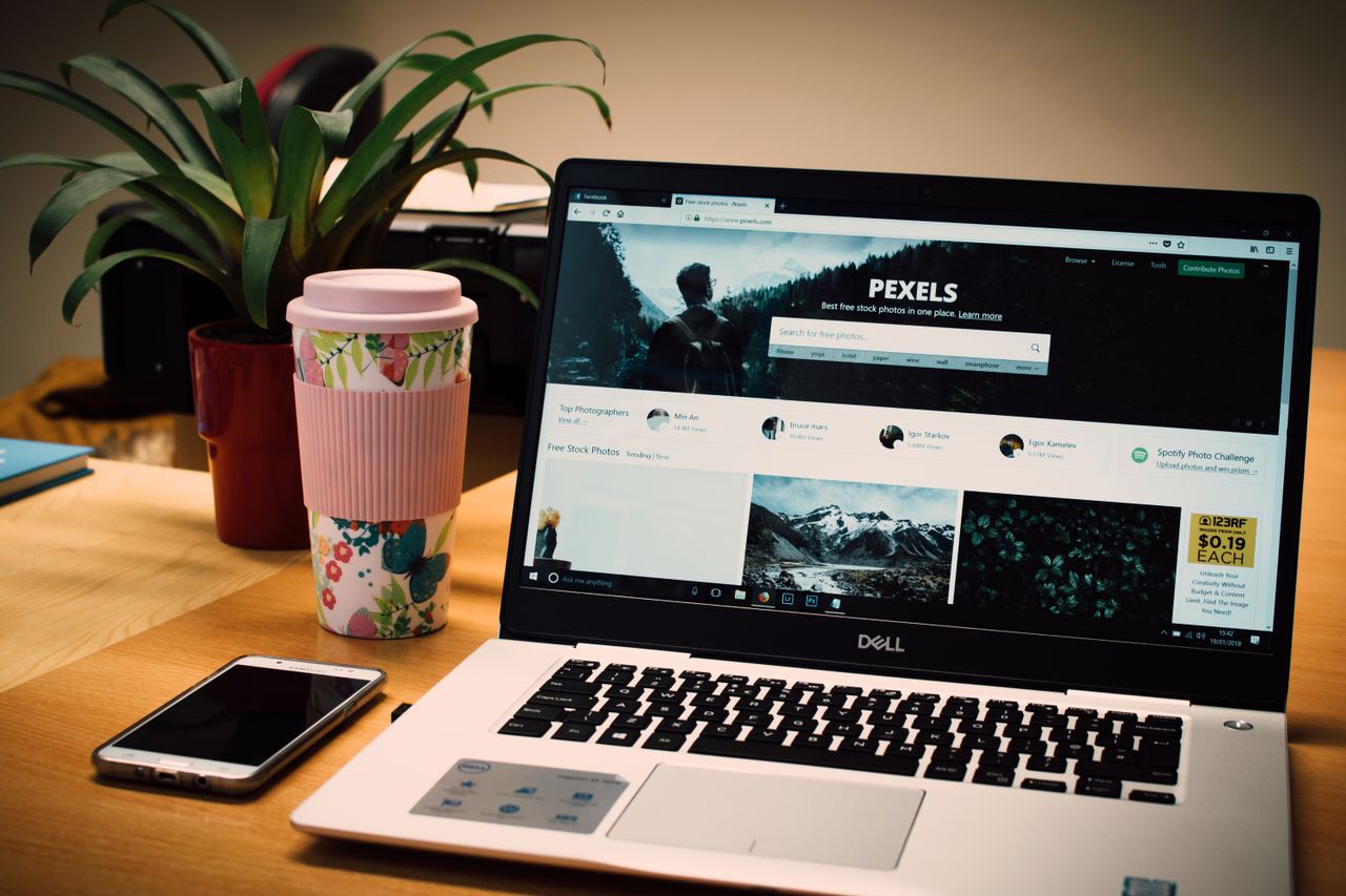 Upravené pracovné miesto s notebookom zobrazujúcim web s fotobankou a smartfónom.